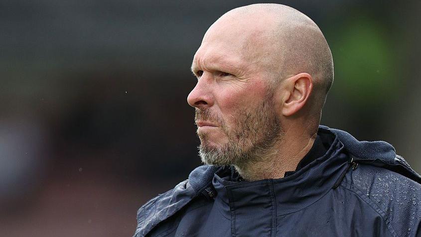 Michael Appleton in his blue club puffer jacket looks on from the touchline during a game