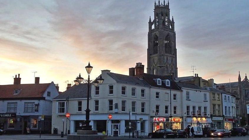 View of a square in Boston at sunset with illuminated shop windows and the Boston Stump tower in the ventre 