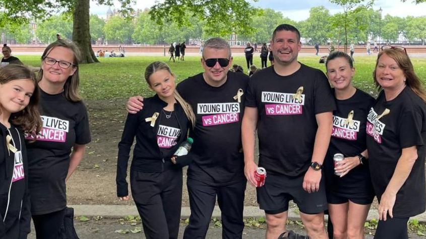Seven members of Abi Quinlisk's family. They are all wearing black T-shirts saying Young Lives vs Cancer. Behind them is a park, showing grass and trees.