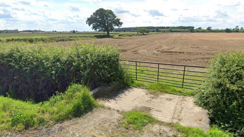 A field with a gate and track running up towards it. It is not clear what, if anything, is growing in the field.
