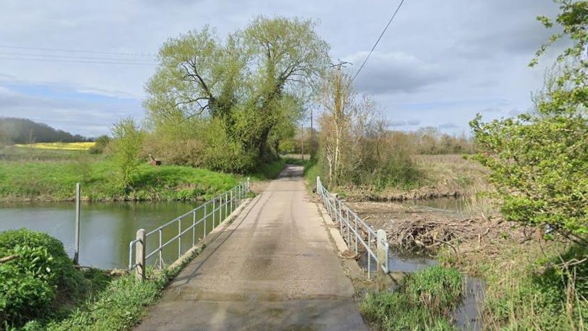 Waterhall Road, a narrow one lane road with a bridge crossing a river. 