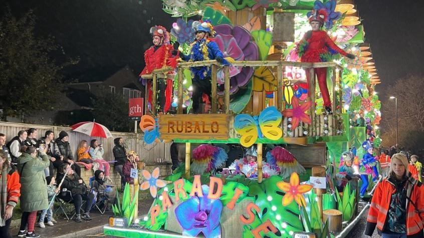 A brightly coloured carnival float decorated with flowers and people in bug costumes. 