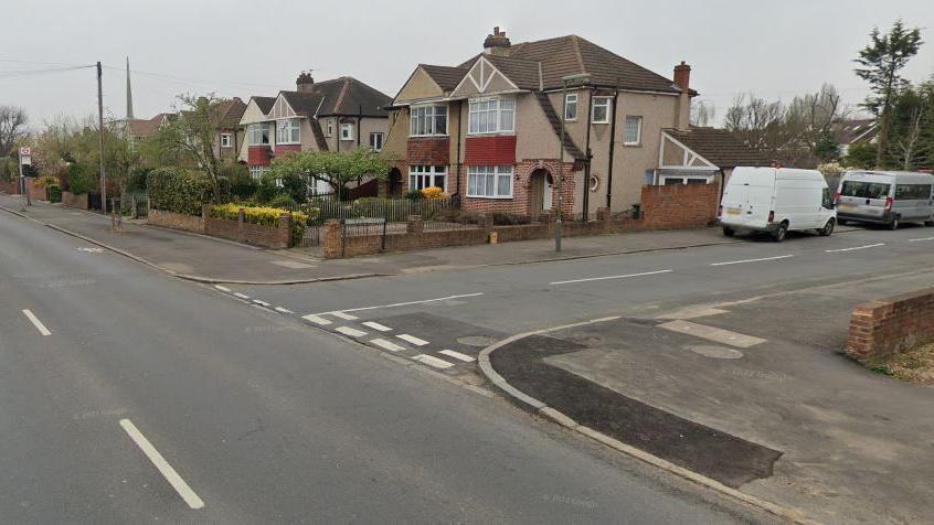 A row of houses on the corner of a t-junction, two white vans are parked down the road 