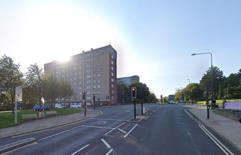 High West Street near its junction with Regent Street. It is a two lane road with traffic lights and a crossroads at the top. There is a big tower block of flats across the road to the left. 