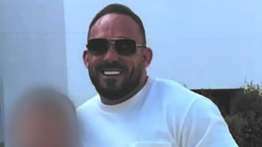 A photograph of Thomas Campbell, who has receding short brown hair, stubble, and is wearing sunglasses and a white t-shirt