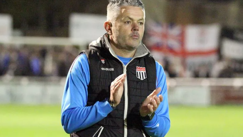 Jerry Gill on the pitch wearing a bright blue sweat shirt and black Bath City gillet, looking solemn and clapping his hands