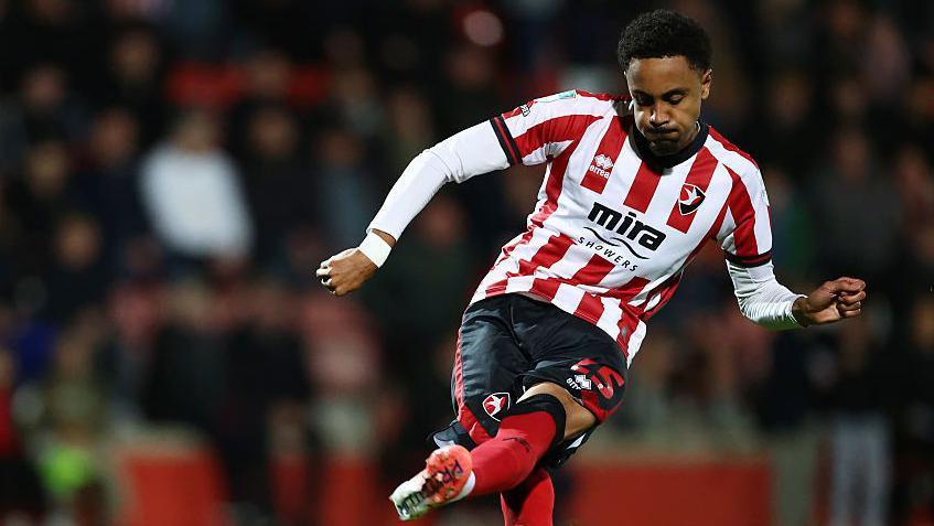 Harrison Sohna scores a penalty kick while playing for Cheltenham Town