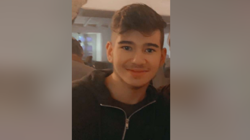 A man wearing a black zip up hoodie smiles into the camera.