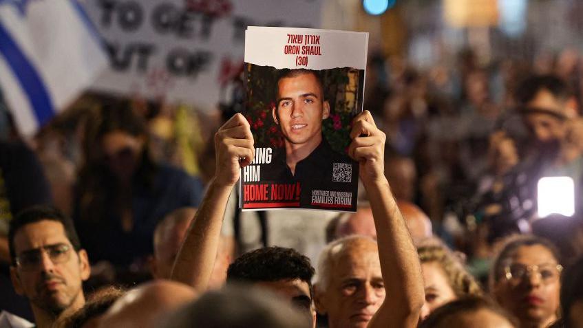 File photo showing a man hold up a poster calling for the release of the body of Israeli soldier Oron Shaul, which was being held by Hamas in Gaza, at a rally in Tel Aviv, Israel (4 November 2023)