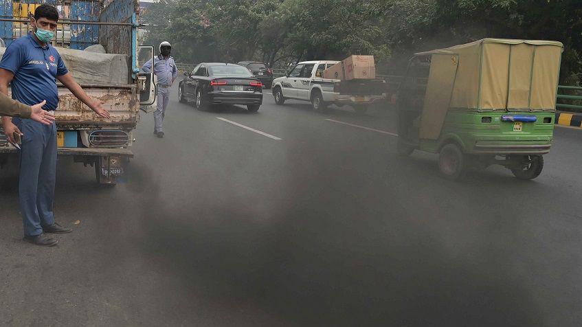 Pakistani security officials checking vehicles producing lots of smoke. 