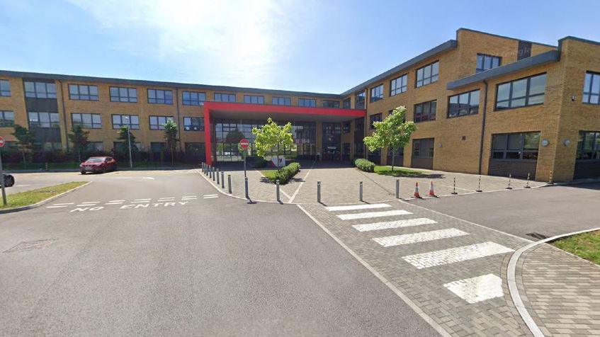 The exterior of Winterbourne School. It is a large brown brick building with lots of windows and a red entrance tunnel.