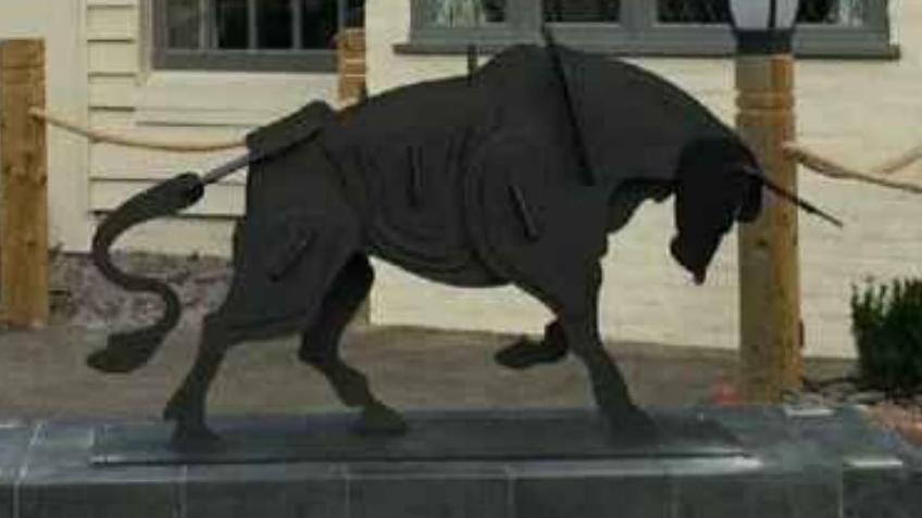 An image of a black metal bull with its head down and hoof lifted, it is placed on a slate plinth