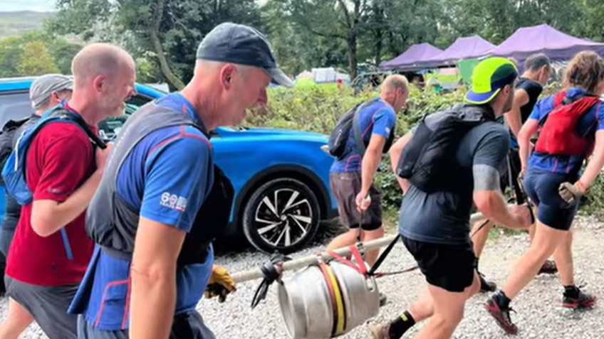 People running carrying a barrel strapped to a pole