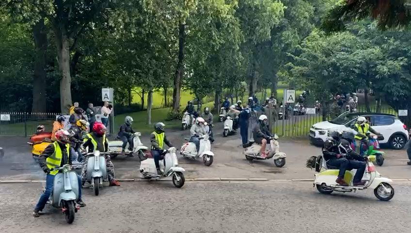 Several riders drive their scooters on the path through a park