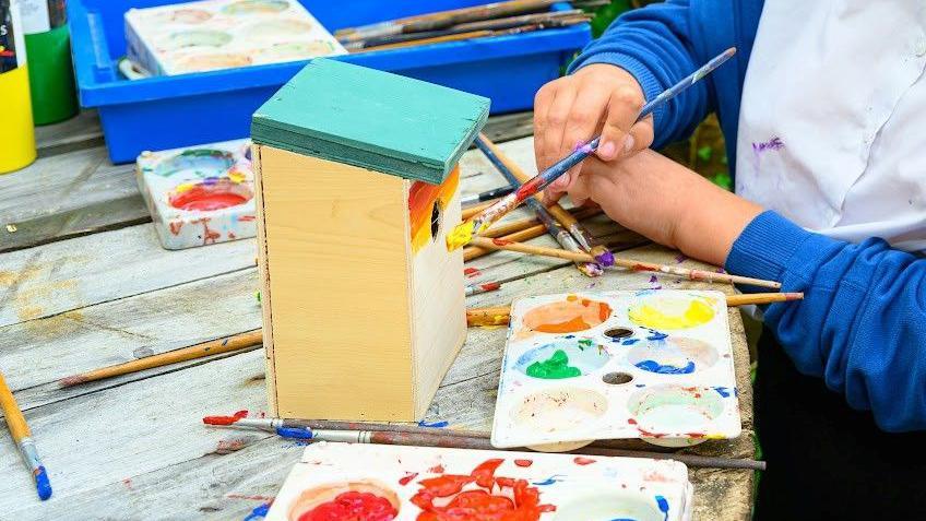 A birdbox being painted by a pair on anonymous schoolchildren