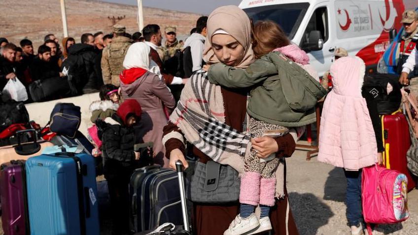 A Syrian woman holding a child waits on the Turkish border in a crowd of refugees