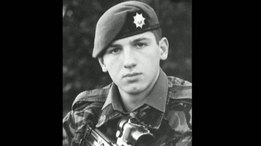 Lance Corporal Alan Forcer in his military uniform. He is wearing a beret with multi-pointed star badge and has on Army camouflage. The sight of the weapon he is holding is just visible in the bottom of the black and white picture.