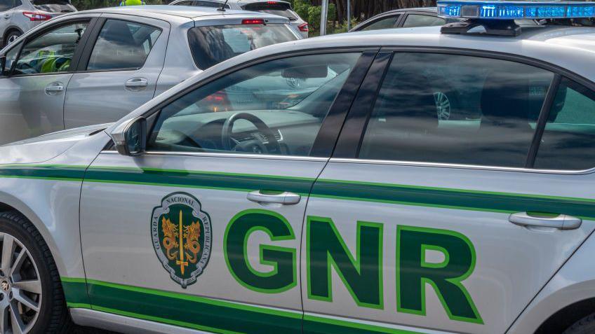 A wide shot of a Republican National Guard police car in Portugal. The car is silver with blue lights and has "GNR" and a crest on its side in green lettering