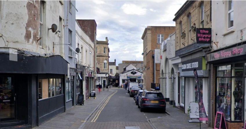 A Google maps street view of West Street in Weston-super-Mare. There are businesses either side of the street and cars parked on one side of the road.