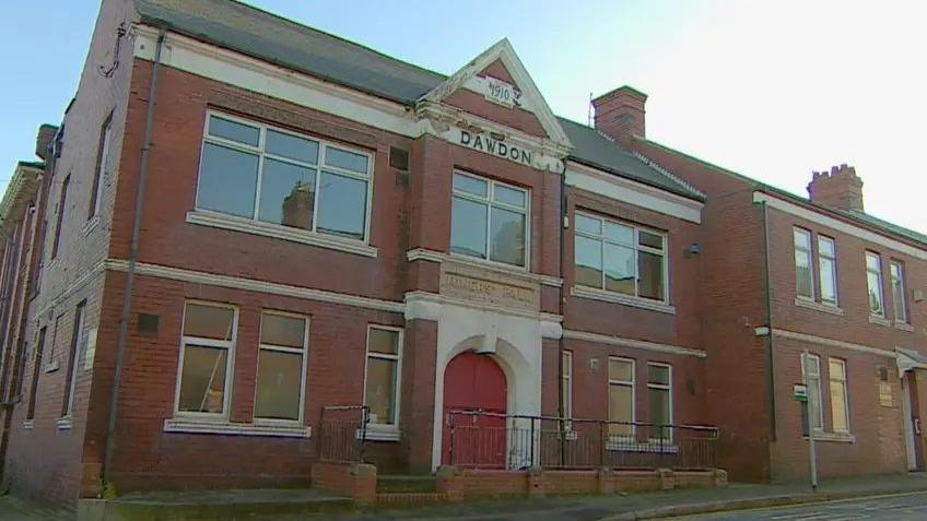 A large two-storey red brick building with a red door. It says "1910, Dawdon" on its front.