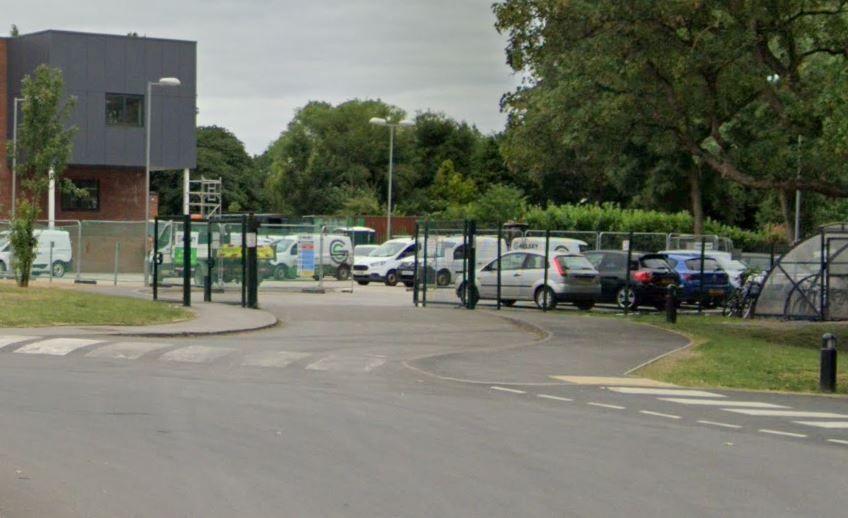 A general view of cars in a car park. There is black mesh fencing and there are trees in the background.