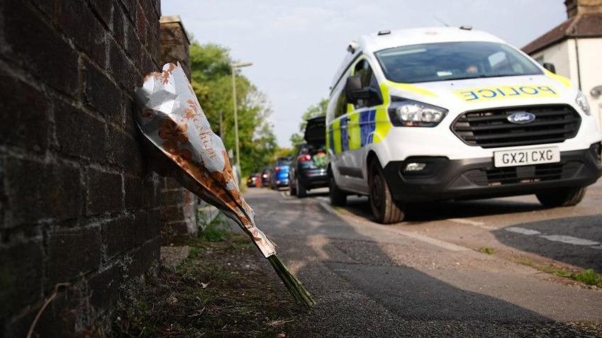 Image shows flowers balanced against a wall near a police car