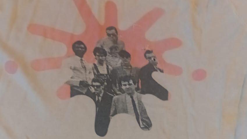 A t-shirt which features a black and white print of The Blockheads. Part of the graphic is missing on one of the band members', after it was chewed and damaged by a dog.