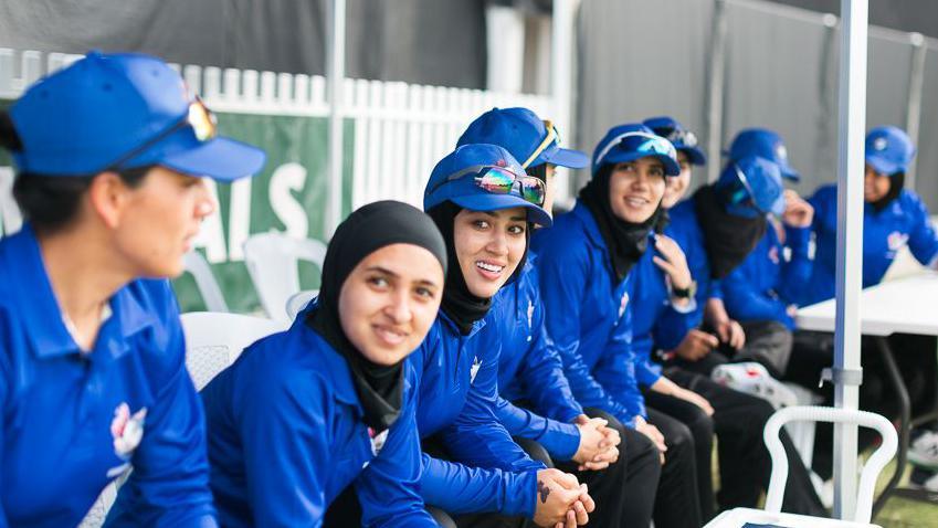 Firooza Amiri and other members of the Afghanistan women's team sit in team kit during their match against Cricket Without Borders