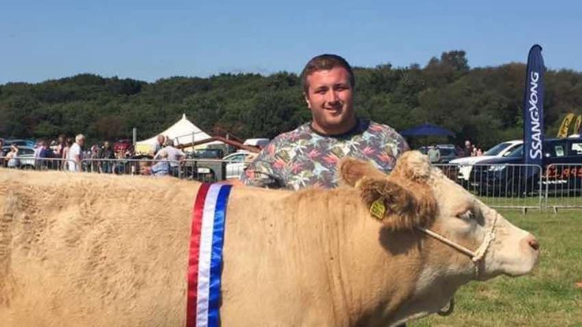 Liam is pictured here with one of his cows at an agricultural show. Liam is wearing a multicoloured t-shirt and has short blonde/brown hair.