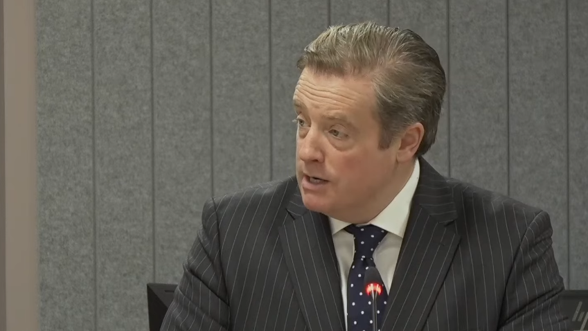 Jamie Dawson KC, wearing a grey pinstriped suit and a blue polka dot tie with a white shirt.