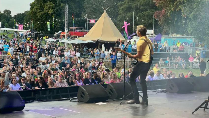A man playing the guitar on a stage in front of people in a park