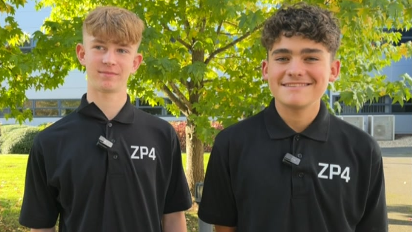 Lewis and Fred stand next to each other, smiling into the camera. They are wearing black polo shirts with ZP4 lettering.