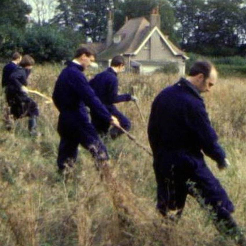 Archive shot of police officers searching through long grass in 1983