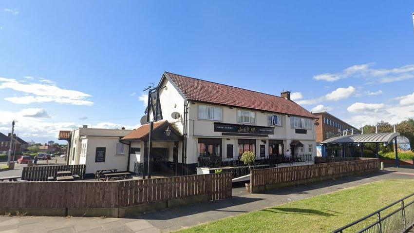 A two-storey white-clad pub building with benches outside.