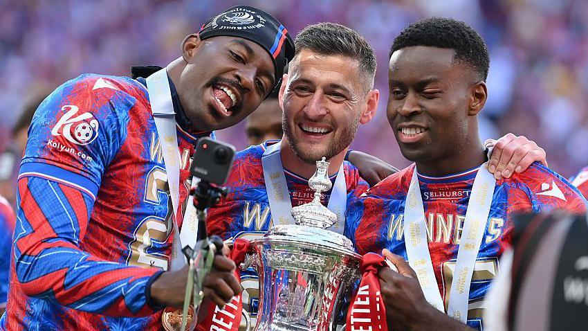  Jean-Philippe Mateta, Joel Ward and Marc Guehi of Crystal Palace pose for a selfie with the FA Cup trophy 