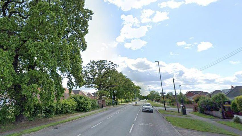 A Google Street View image of Doncaster Road lined with houses, trees and greenery. A silver car is shown on the road. 