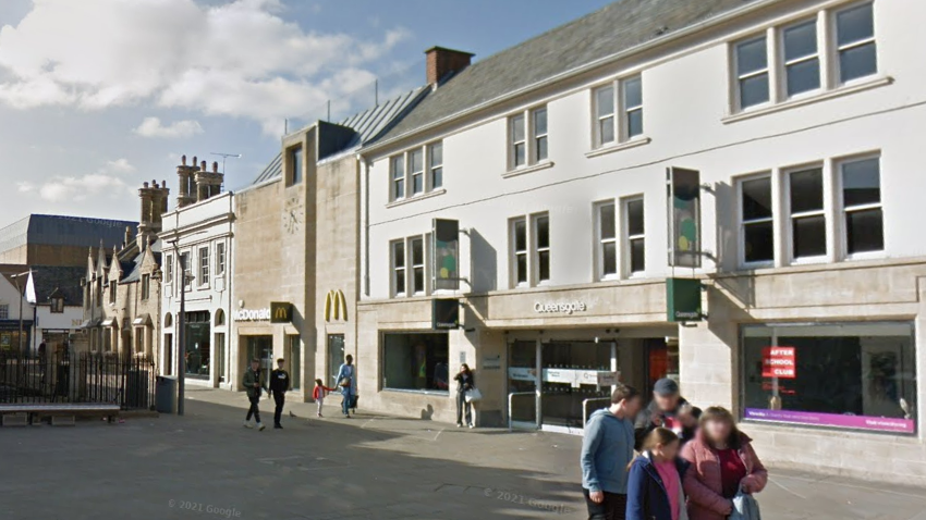 Exterior picture of Queensgate - white building with rectangle windows and a big yellow M on the wall for McDonald's and people walking in front of it