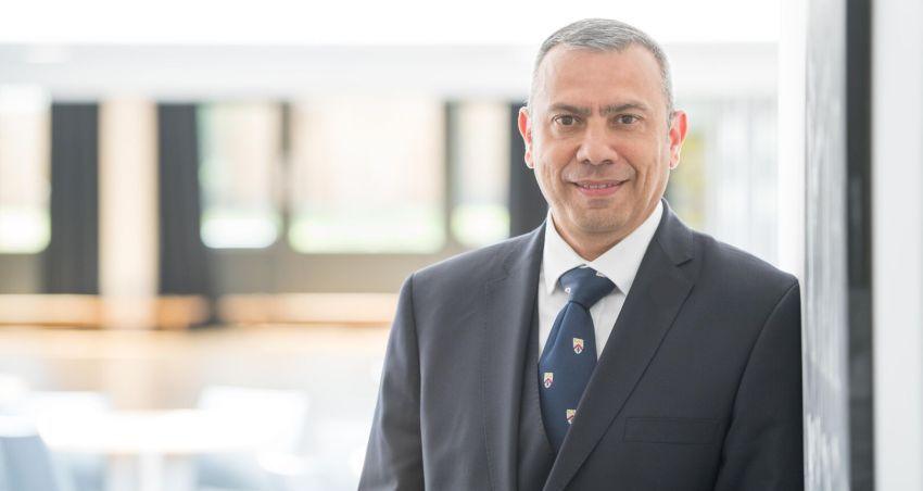 Martin Serrão in a navy suit, white shirt and navy tie stands to the left hand side smiling at the camera.