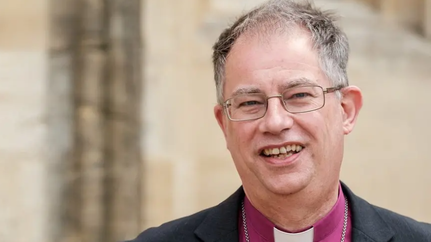 Bishop Steven smiling at the camera has grey hair, is wearing glasses and has a purple clerical shirt.