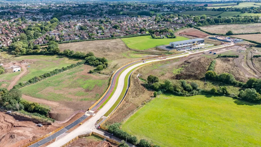 An aerial view of the partially competed Orchard Grove development on the outskirts of Taunton. A new primary school stands in the background, with a long road snaking through fields towards it. 