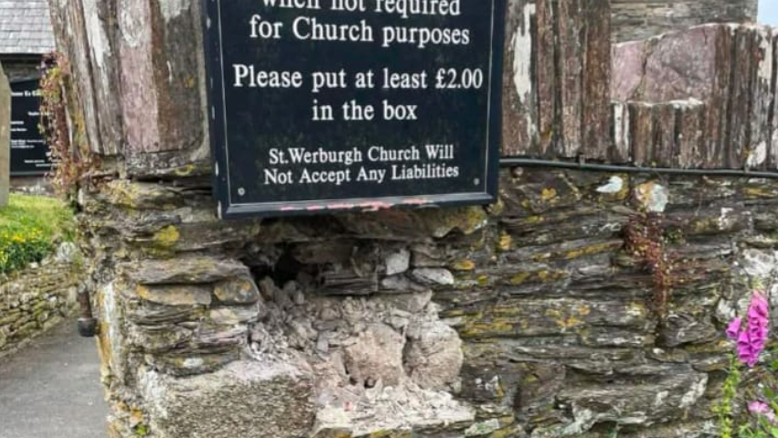 A stone wall with a hole and a sign above it.