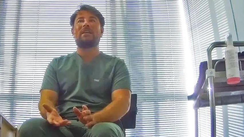 A man wearing medical scrubs is seen talking to someone off-camera.