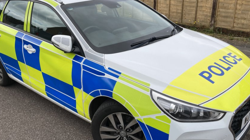 The side view of a police car with blue and yellow markings on the panels, and the word police across the bonnet