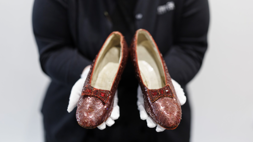 A gallery assistant holds movie character Dorothy's ruby slippers, worn by US actor and singer Judy Garland in the film 'The Wizard of Oz',