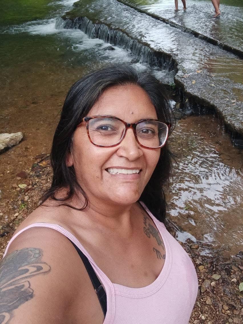 Reyna Gillahan, who died in a munitions factory explosion, tanks a selfie in a pink tank top and glasses in front of a small waterfall.