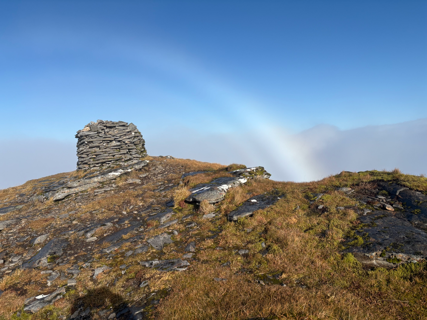 A fog bow on a sunny day, over a hilly and grassy area