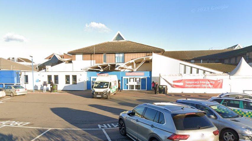 A Google Street image of the front of a hospital. There is an ambulance parked in front of sliding doors.