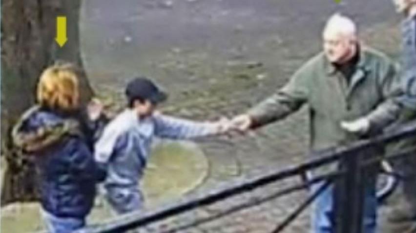 CCTV showing Sergei Skripal handing bread to a young boy while they feed ducks. Sergei is in a green coat and the young boy wears a dark cap and grey top.