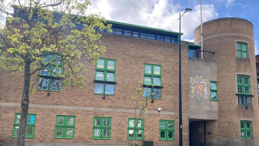 Luton Crown Court: a brown-bricked building with green-framed windows. A sign above the entrance says "CROWN COURT".