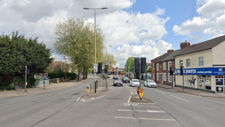 A city dual carriageway showing cars stopped at the traffic lights and a betting shop.  